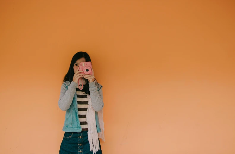 a woman taking a picture of herself with a camera, inspired by Wes Anderson, pexels contest winner, postminimalism, pink and orange, wearing denim, young asian girl, dafne keen