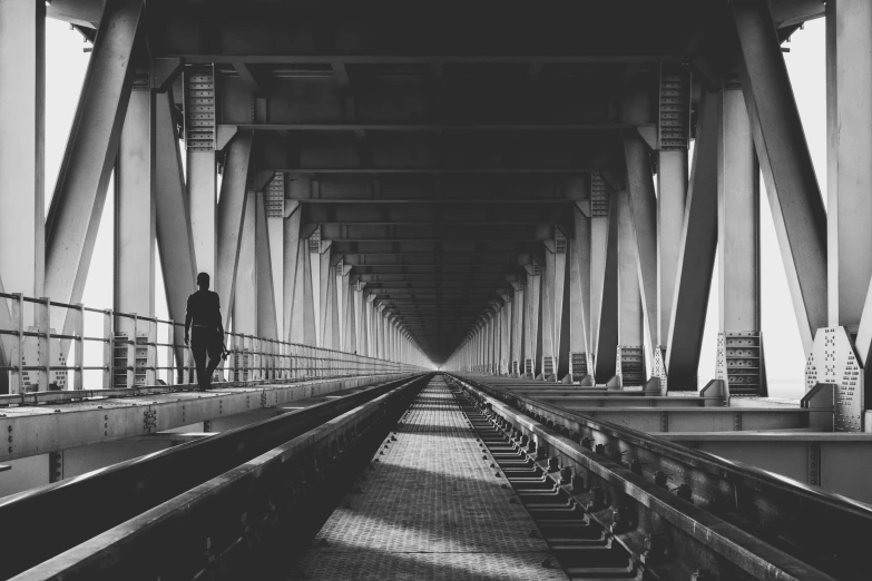 a black and white photo of a man standing on a bridge, by Karl Buesgen, unsplash contest winner, symmetrical!! sci-fi, long hallway, photography alexey kurylev, train far