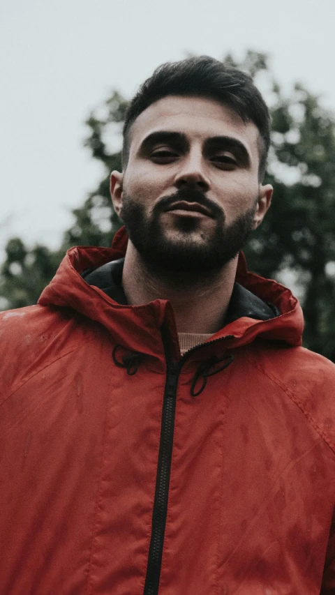 a man with a beard wearing a red jacket, an album cover, inspired by Kyle Lambert, pexels contest winner, hurufiyya, low quality grainy, outdoor photo, looking confident, hooded