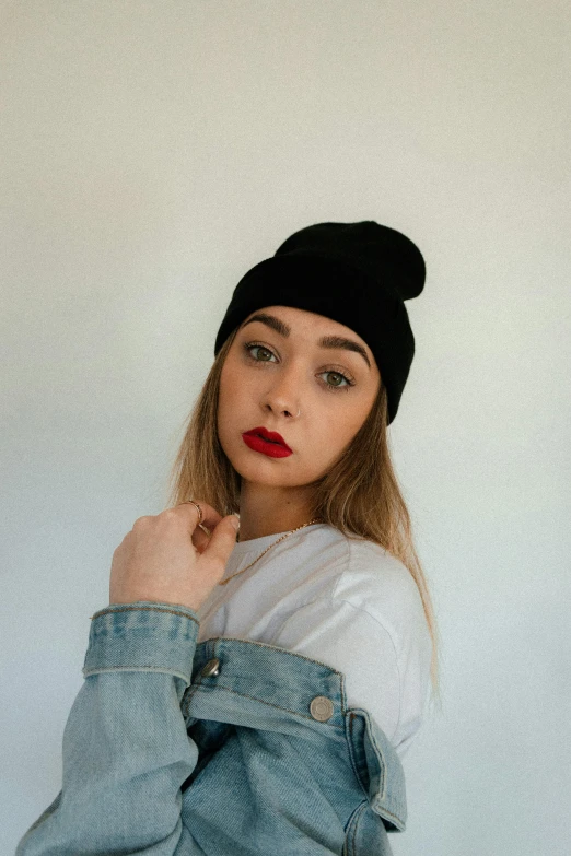 a blonde girl posing in front of a white wall wearing a black beanie