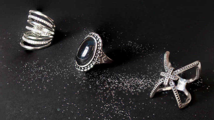 a couple of rings sitting on top of a table, black and silver, ancient fairy dust, product photography, silver