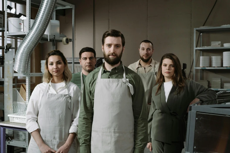 a group of people standing next to each other in a kitchen, a portrait, by Andrew Stevovich, pexels contest winner, wearing human air force jumpsuit, small manufacture, promotional image, serious business