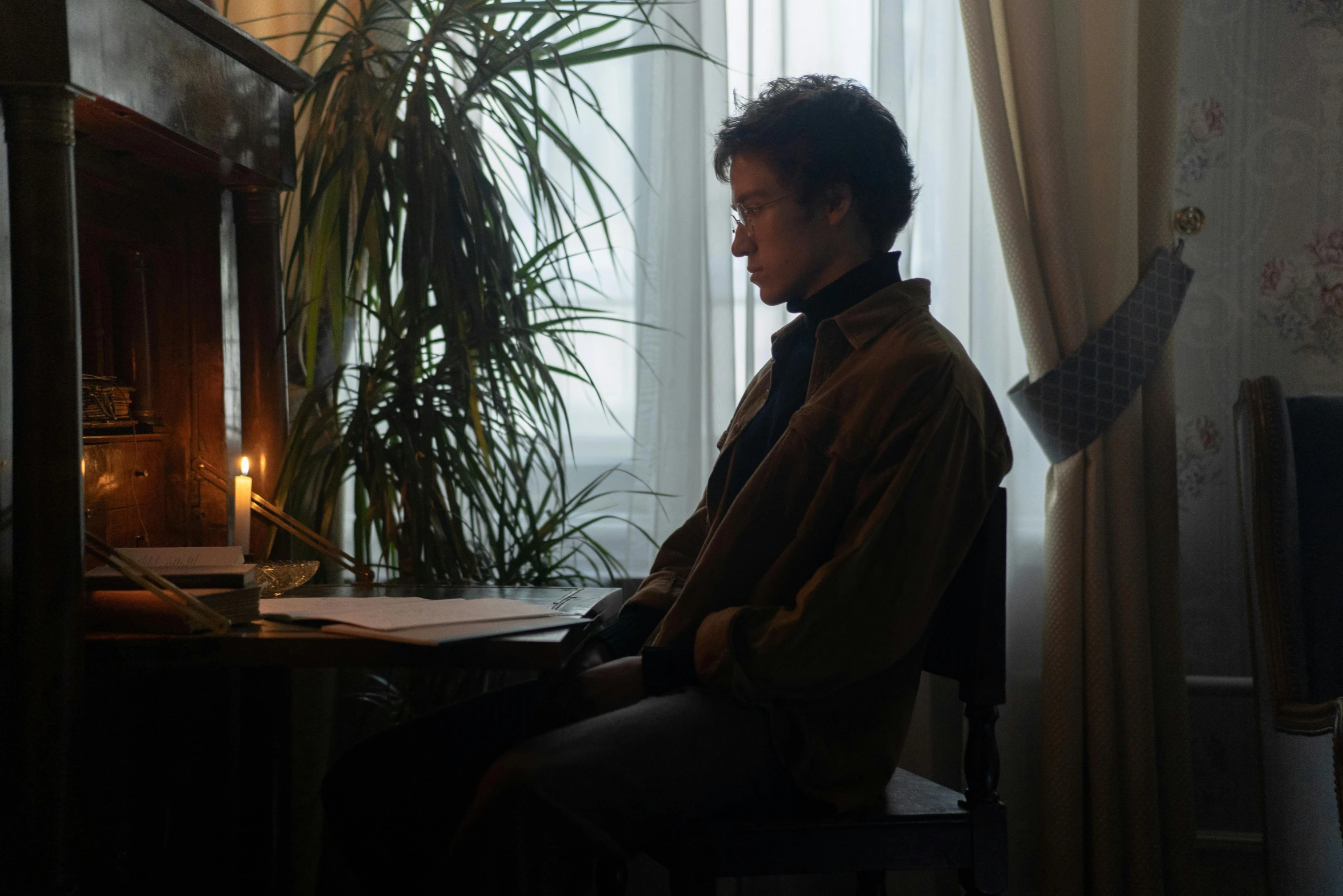 a man sitting in front of a desk next to a potted plant