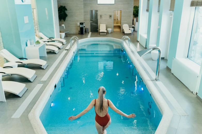 a person in a red swimsuit standing in a pool next to lounge chairs