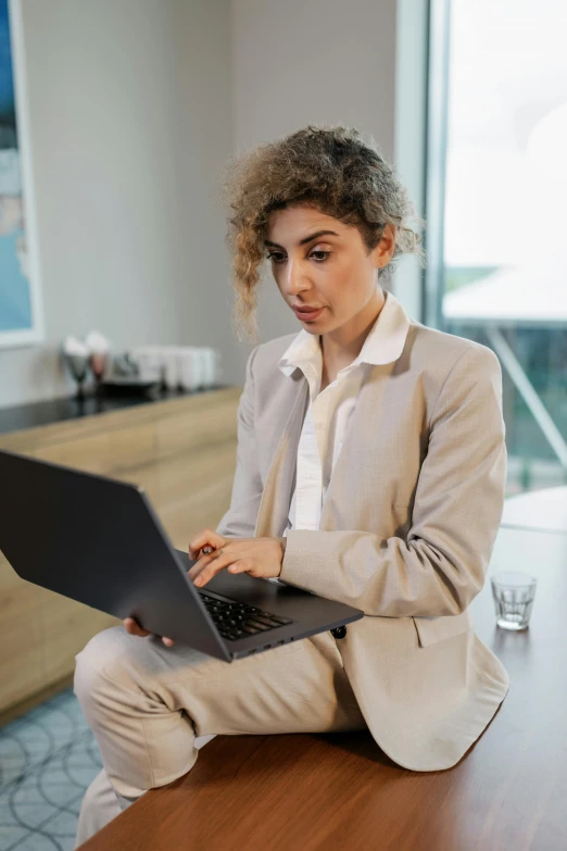 a woman sitting on a table with a laptop, wearing a fancy jacket, trending on attestation, multiple stories, technical