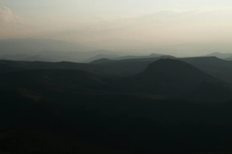 a person flying a kite on top of a mountain, inspired by Andreas Gursky, les nabis, black mountains, dusk lighting, very hazy, view from helicopter