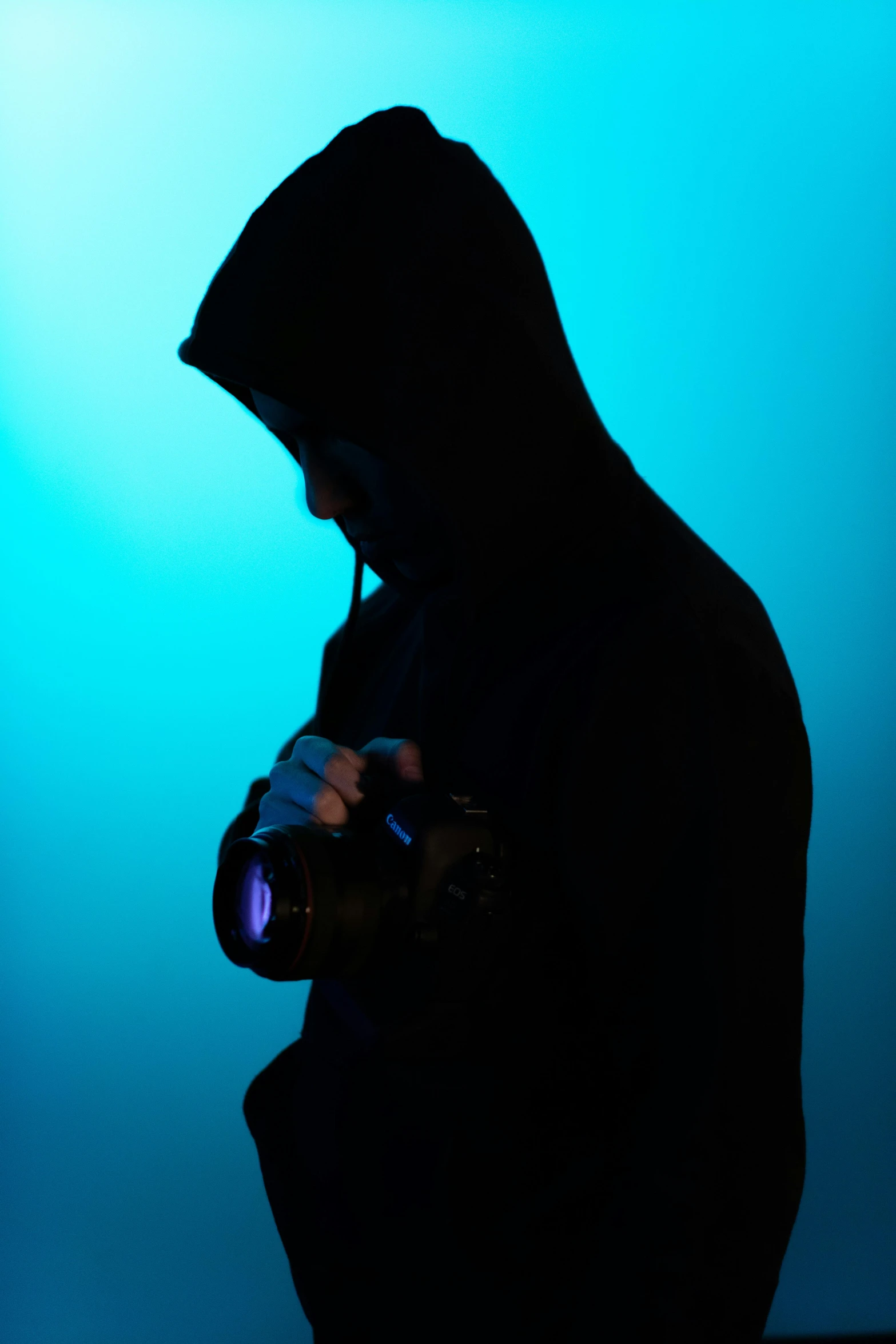 a silhouette of a person in a hoodie holding a camera, by Joseph Severn, art photography, blue backlight, concerned, color photograph, studio shot