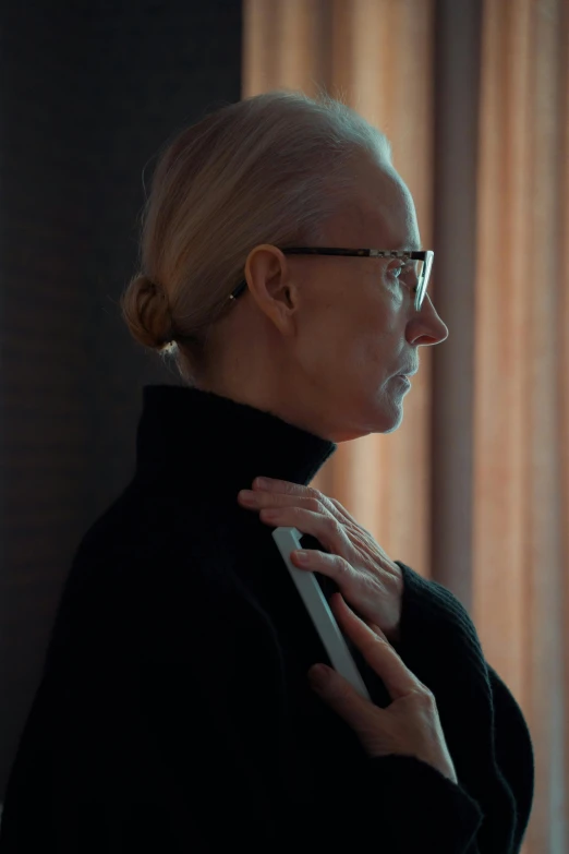 a woman adjusting her tie in front of a window, inspired by Sigrid Hjertén, black turtleneck, portrait tilda swinton, worksafe. cinematic, standing in a dimly lit room