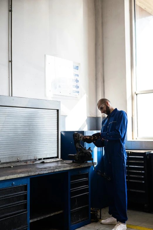 a man working on a machine in a factory, a portrait, arbeitsrat für kunst, wearing blue robe, white wall coloured workshop, add text: auto repair, trending photo