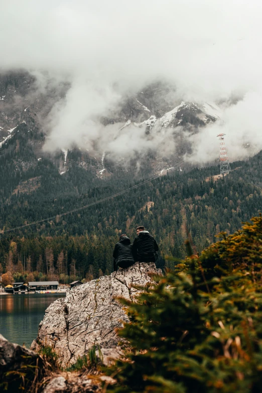 a man with a backpack sits on a cliff with a view of a mountain range in the background