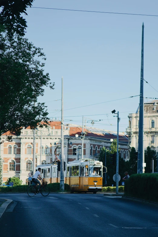 a yellow train traveling down a street next to a tall building, danube school, on a great neoclassical square, trams ) ) ), high quality image, 🚿🗝📝