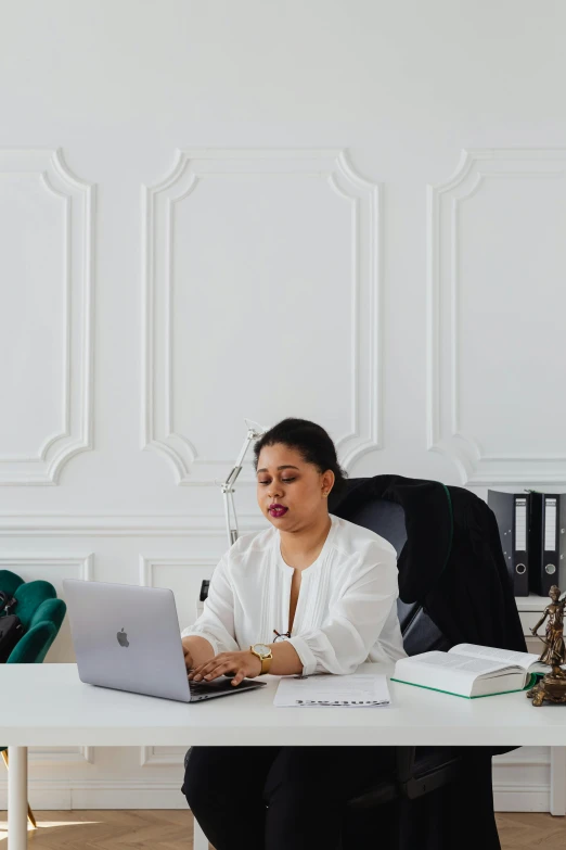 a woman sitting at a desk with a laptop, inspired by Ruth Jên, female lawyer, in white room, riyahd cassiem, ornate designs on desk