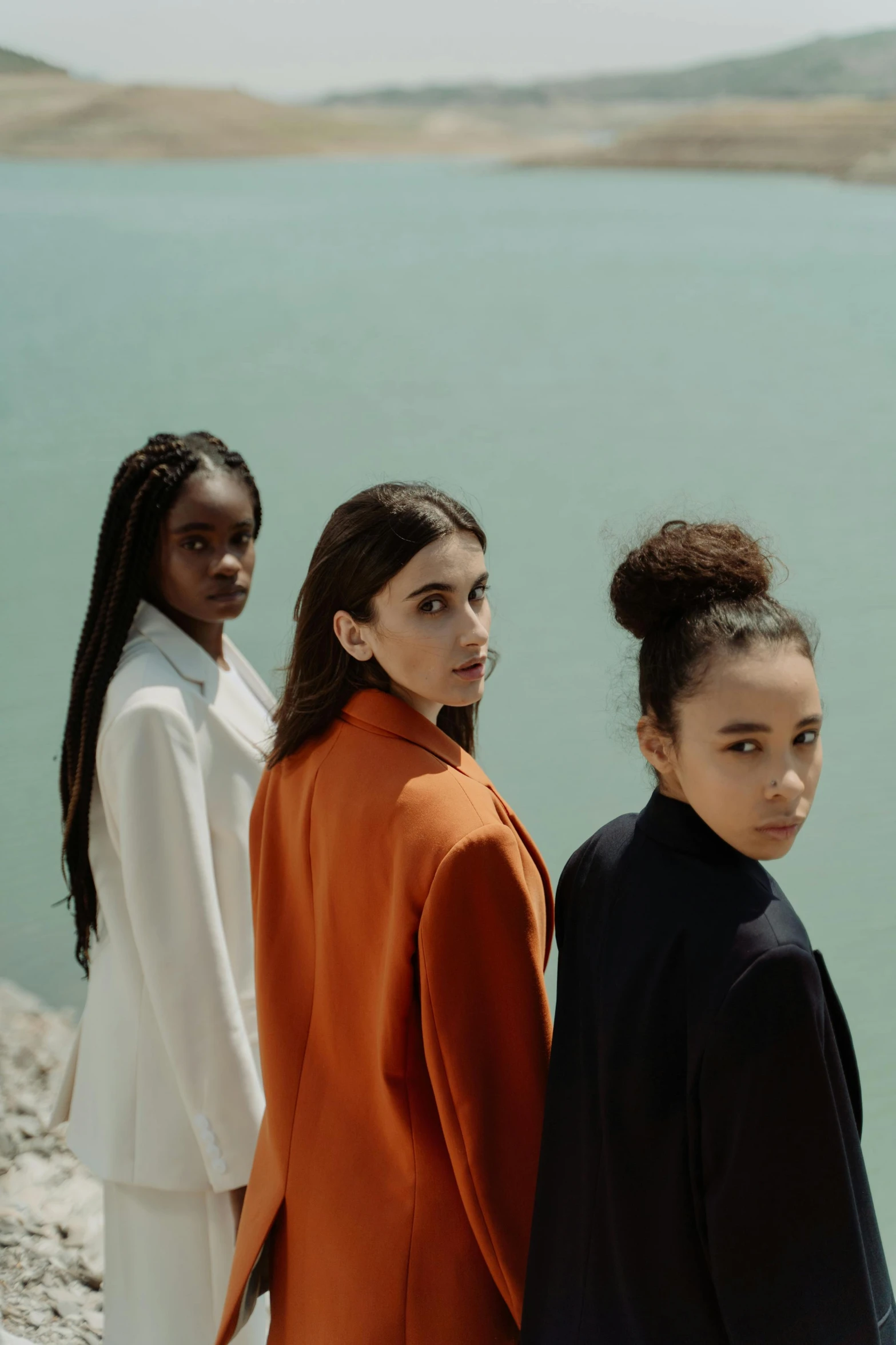 a group of women standing next to each other near a body of water, an album cover, by irakli nadar, trending on pexels, girl in suit, serious faces, color block, ( brown skin )