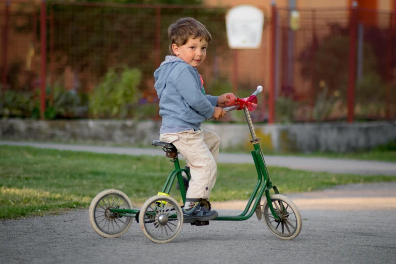 a young boy riding a green tricycle down a street, an album cover, by Jakob Gauermann, dribble, recreation, high quality upload, taken in the early 2020s, profile image