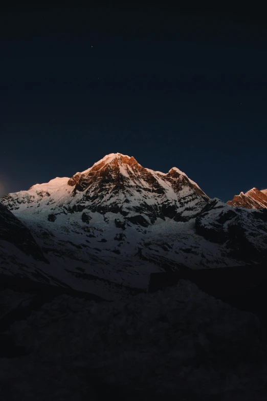 the moon is setting over a mountain peak