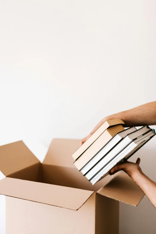 a woman holding a stack of books in a cardboard box, pexels contest winner, instagram post, with a white background, background image, lachlan bailey