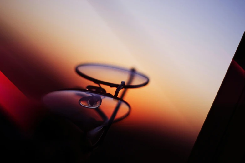 a pair of glasses sitting on top of a table, by Thomas Häfner, art photography, ((sunset)), tear drop, thin dof, flight