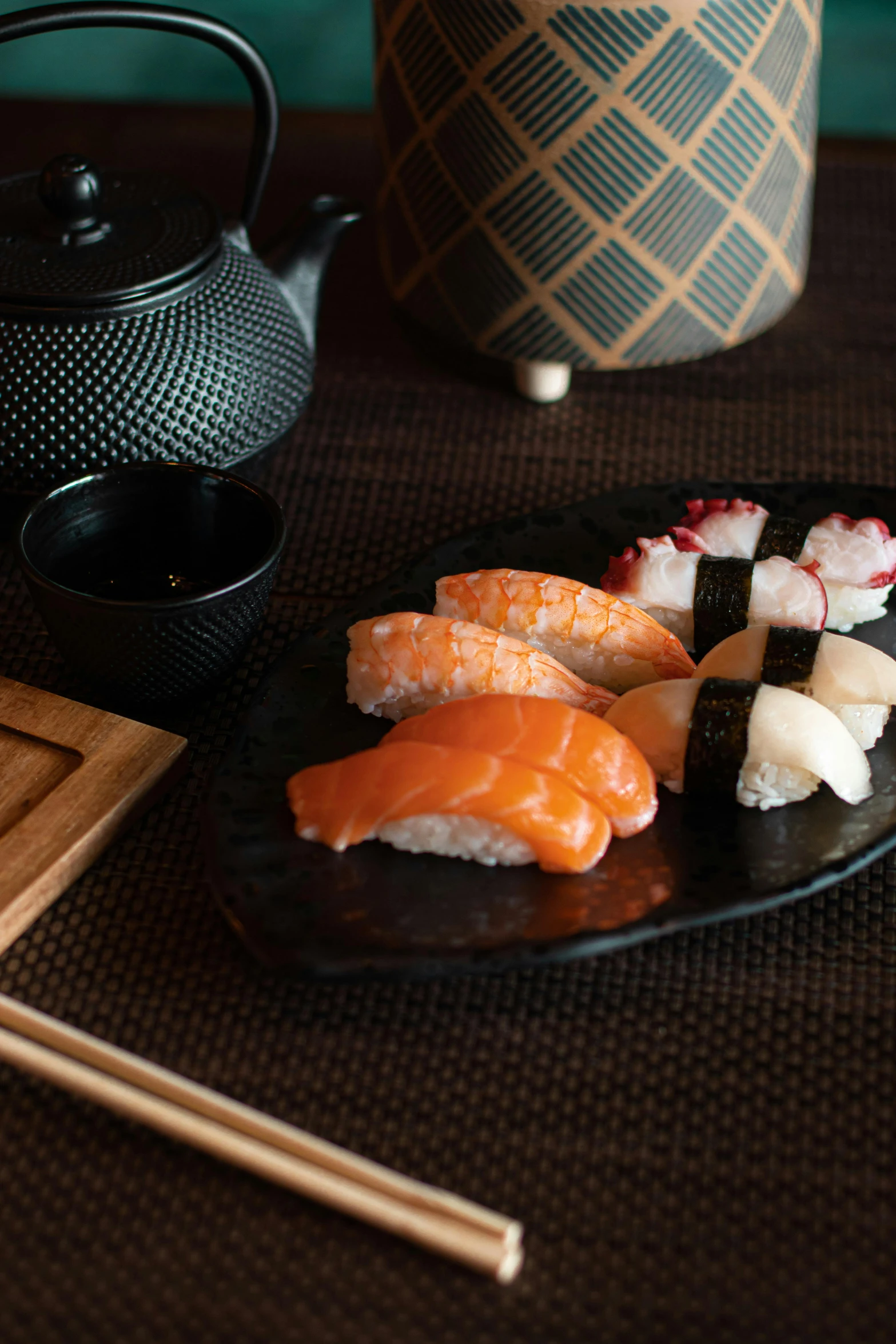 plates of sushi on the table with an oriental teapot behind them