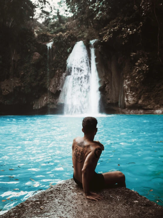 a man sitting on a rock in front of a waterfall, by Byron Galvez, pexels contest winner, sumatraism, crystal clear blue water, loin cloth, facing away from camera, instagram story