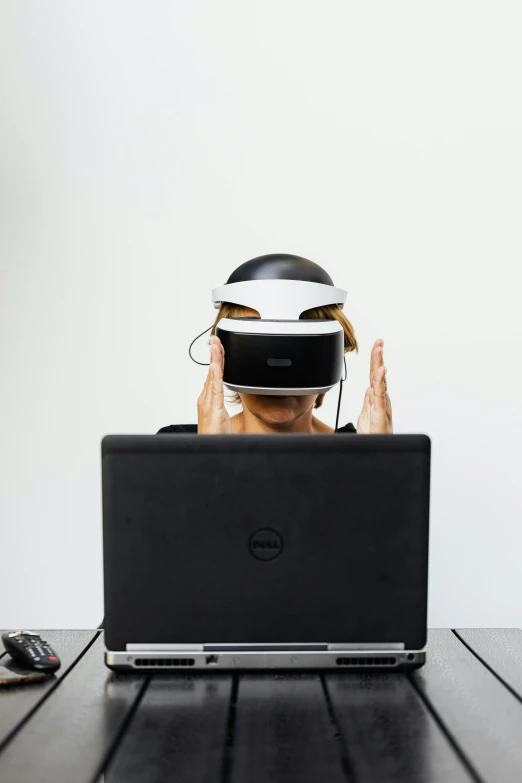a man sitting at a table with a laptop in front of him, a hologram, inspired by Zhu Da, hypermodernism, wearing a vr headset, back facing the camera, no - text no - logo, cardboard