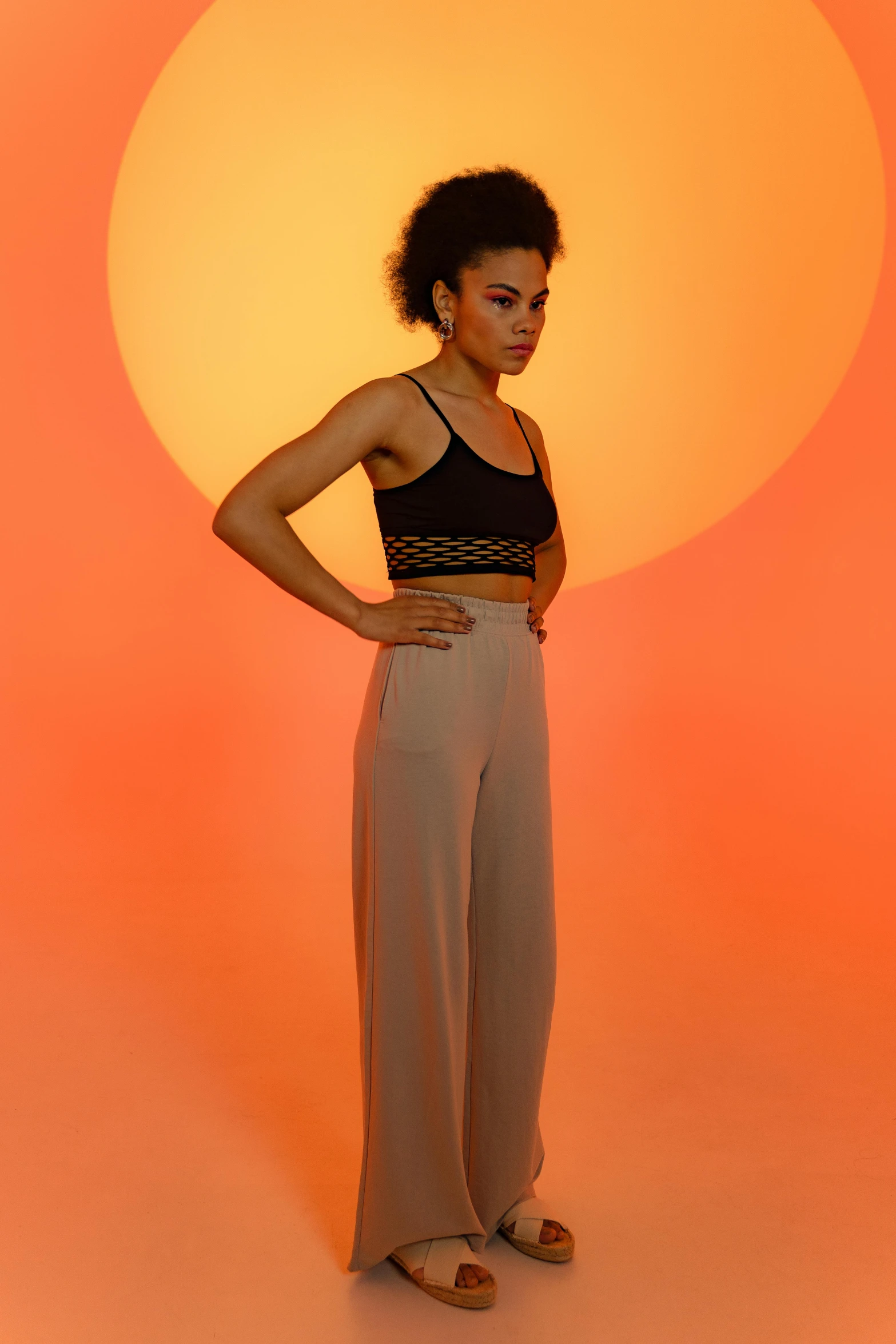 a woman standing with her hands on her hips, trending on pexels, arabesque, warm orange lighting, wearing a crop top, at a fashion shoot, pastel'