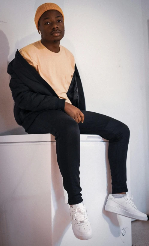 a man wearing a yellow beanie and black sweatpants is sitting on top of a wall