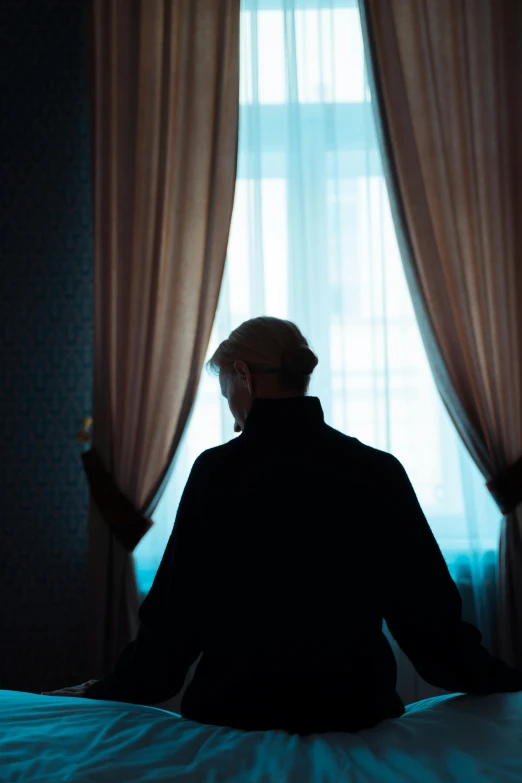 a man sitting on a bed looking out the window