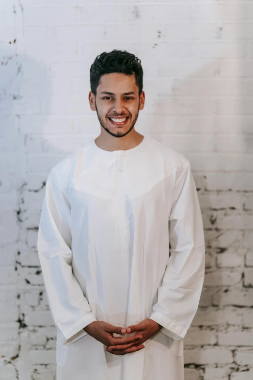 man wearing white traditional clothing, standing in front of brick wall