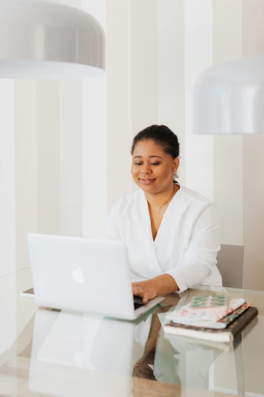 a woman sitting at a table with a laptop, all white, riyahd cassiem, cindy avelino, elegantly