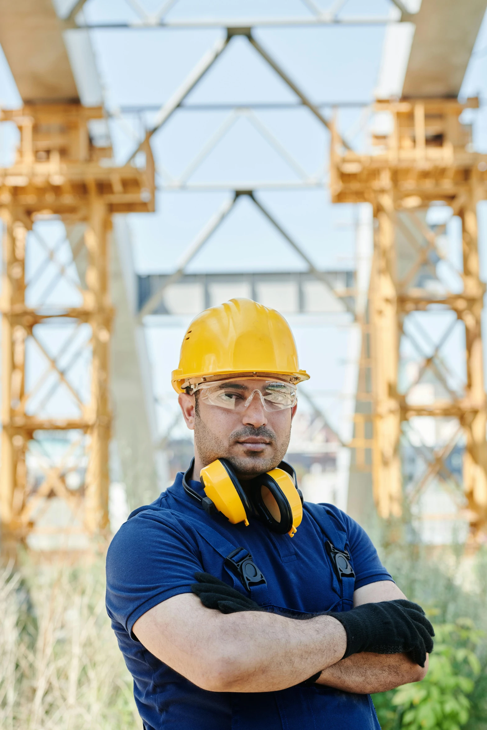 a man wearing a hard hat standing in front of a bridge, a portrait, pexels contest winner, truss building, avatar image, wearing goggles, center of image