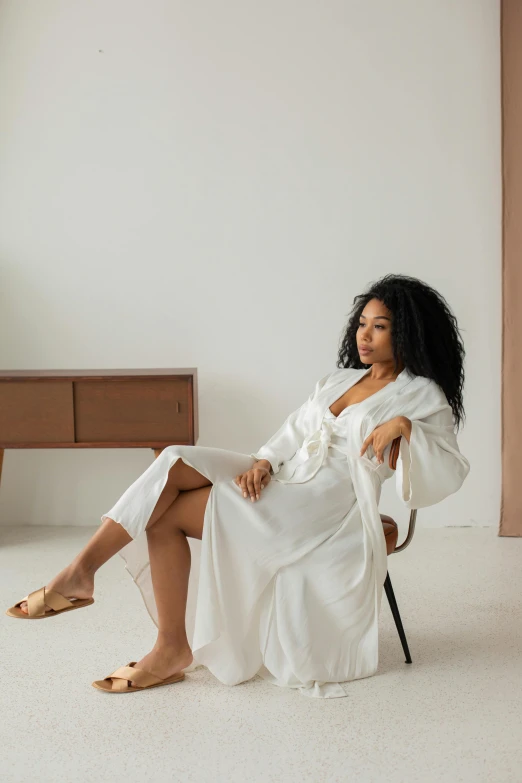 a woman in a white robe is sitting in a chair, inspired by Esaias Boursse, unsplash, tessa thompson, sleepwear, sza, curated collection