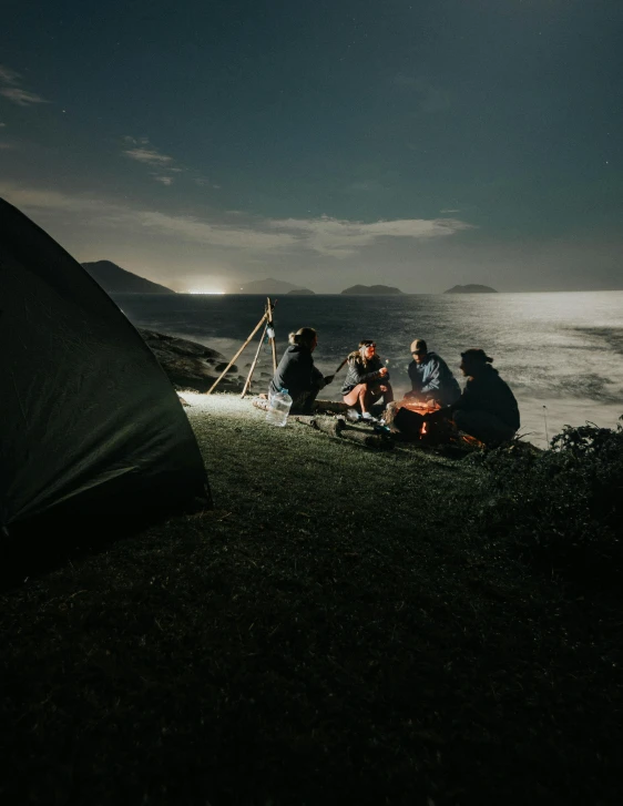 a group of people sitting around a campfire, by Kristian Zahrtmann, pexels contest winner, overlooking the ocean, tent, fishing, night time footage