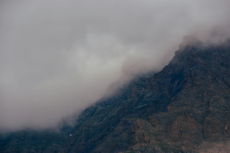 a large mountain side with a single airplane flying low by