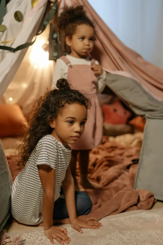 a couple of little girls sitting on top of a bed, pexels contest winner, interior of a tent, african american girl, in an attic, girl standing