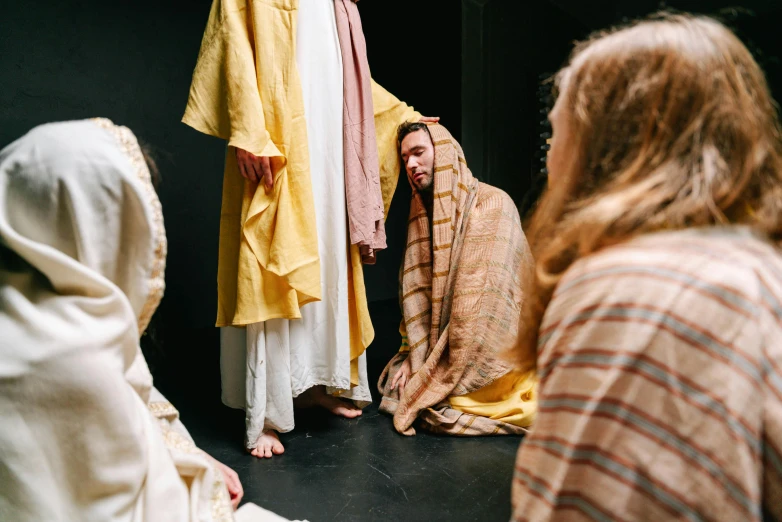 a man standing in front of a group of people, by Everett Warner, trending on unsplash, renaissance, yellow robe, [ theatrical ], jesus of nazareth, kneeling