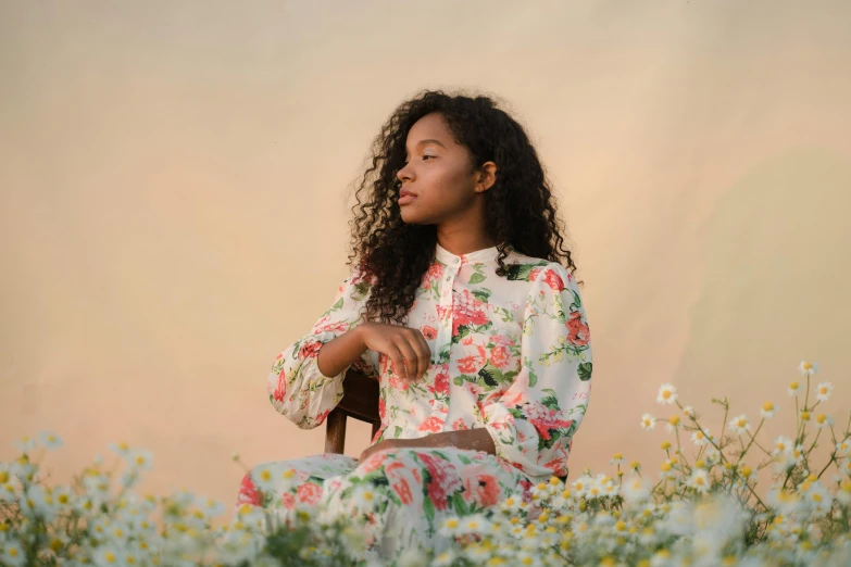 a woman sitting in a field of flowers, by Lily Delissa Joseph, trending on pexels, renaissance, black teenage girl, sitting on chair, patterned clothing, soft evening lighting