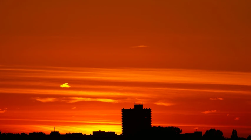 a plane flying over a city at sunset, a picture, orange, silhouette :7, utrecht, fiery