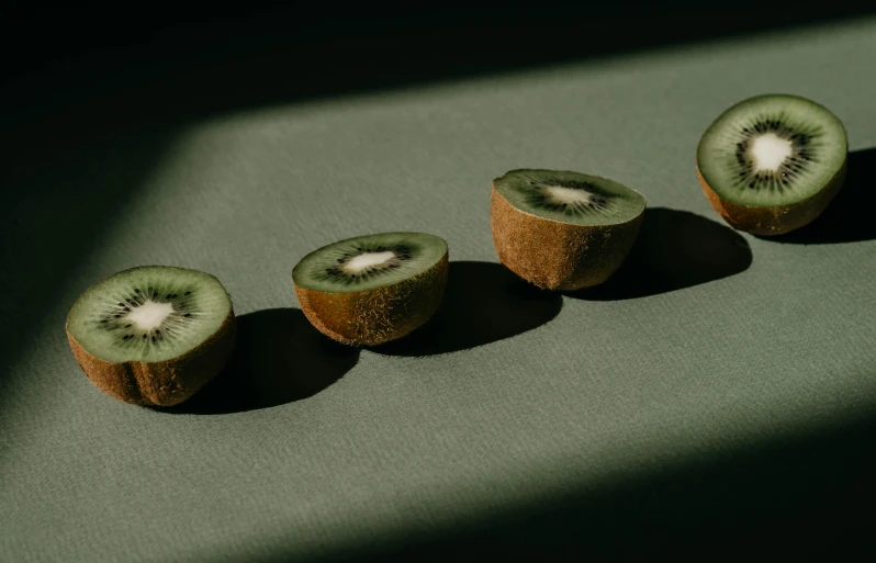 a group of kiwi slices sitting on top of a table, a still life, by Emma Andijewska, trending on pexels, visual art, olive green, in a row, looking across the shoulder, in the spotlight