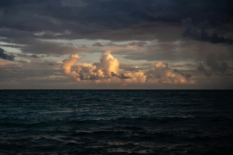 a cloudy sky hangs over the ocean in an evening