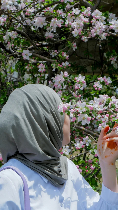 a woman standing in front of a flowering tree, by Maryam Hashemi, shutterstock, she is eating a peach, hands shielding face, ap news photo, slide show