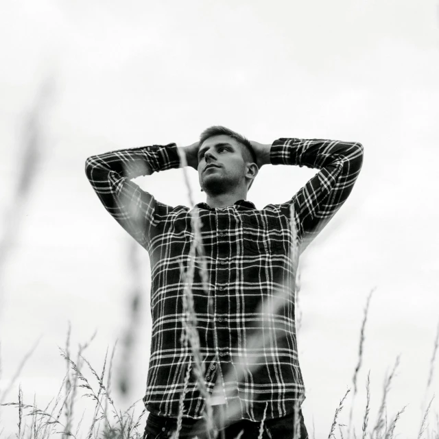 a man standing in a field of tall grass, a black and white photo, unsplash, wearing plaid shirt, grim fashion model looking up, isolated, meditative