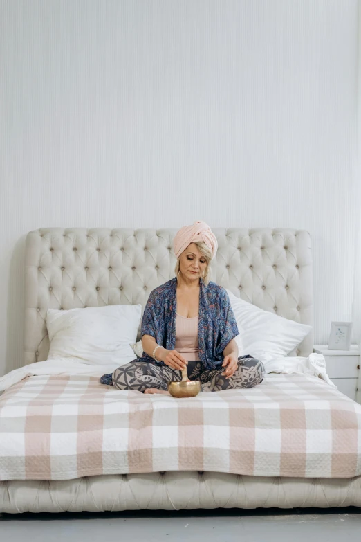 a woman sitting on top of a bed in a bedroom, kundalini energy, turban, holding a candle holder, pink zen style