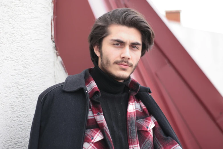 a man stands in front of a red wall wearing a black shirt