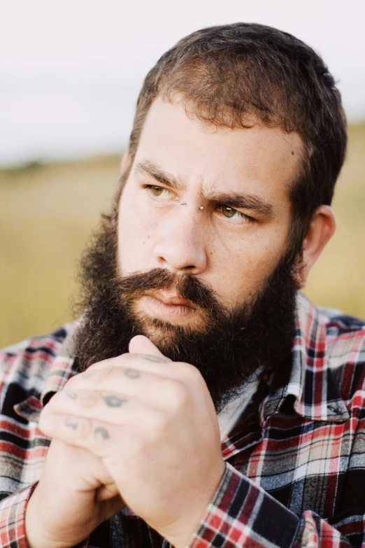 a bearded man with tattoos sitting in an empty field