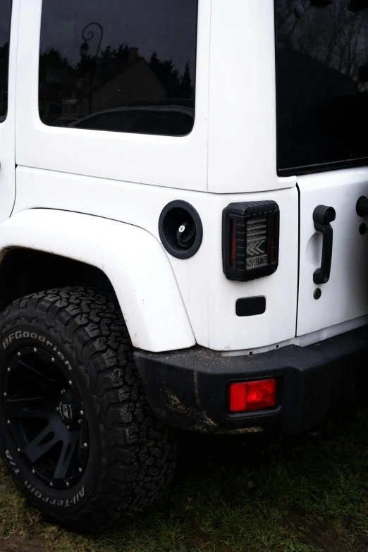 the white jeep with the black wheels is parked on grass