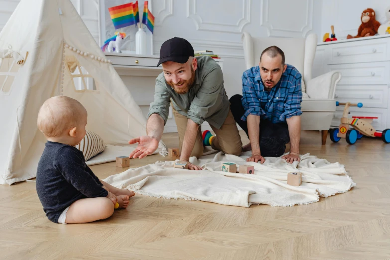 a man sitting on the floor playing with a baby, inspired by The Family Circus, pexels contest winner, two buddies sitting in a room, with a kid, lgbtq, architect