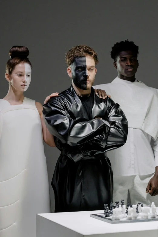a group of people standing around a chess board, an album cover, afrofuturism, white facepaint, black clothing, ( ( theatrical ) ), a portrait of issey miyake