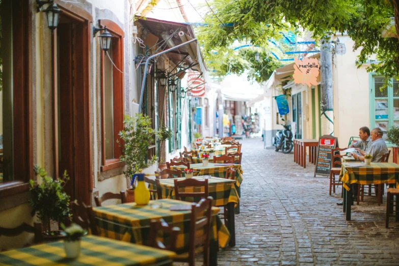 a narrow street lined with tables and chairs, a photo, greek setting, profile image, fan favorite, 90s photo