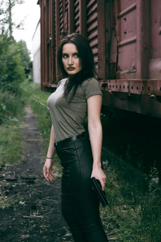 a beautiful young woman standing next to a train, an album cover, by Lucia Peka, pexels contest winner, leather pants, dark hair and makeup, wearing pants and a t-shirt, militaristic
