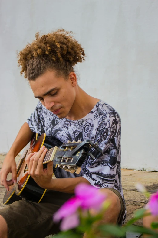 a young man sitting in front of flowers and playing an acoustic guitar